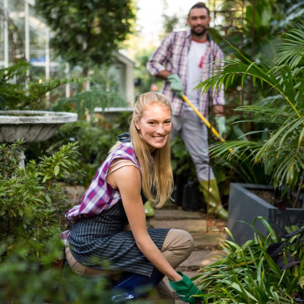 Portrait of happy young female gardener with colleague in community garden